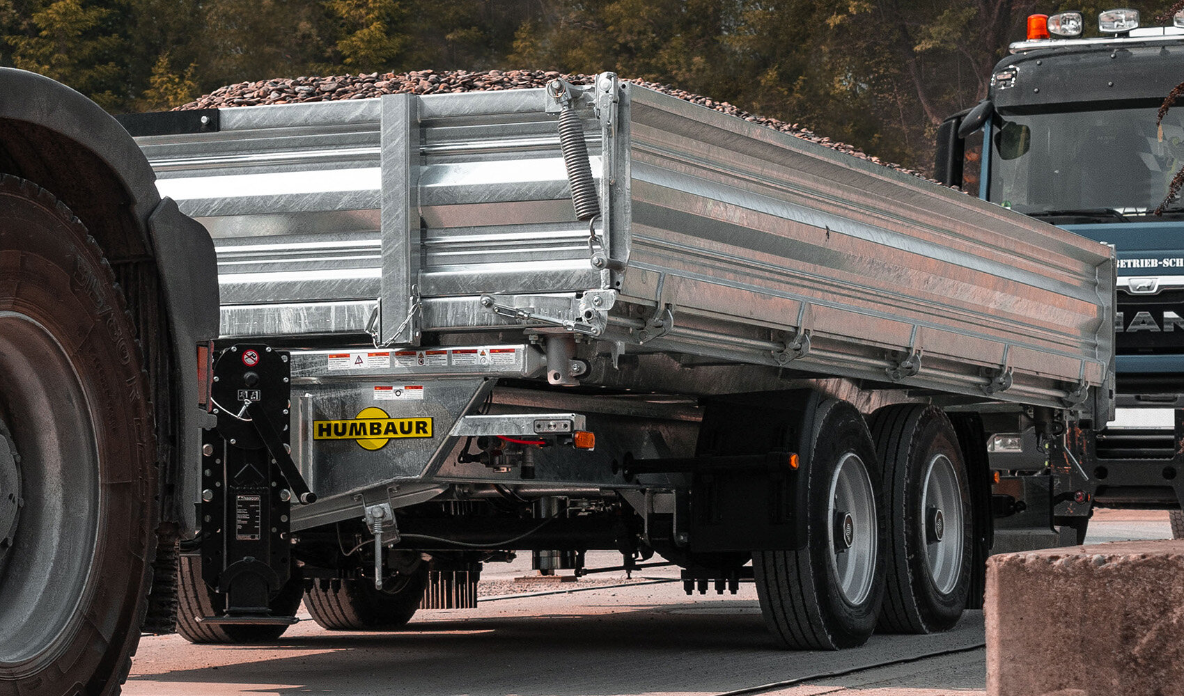 Une remorque de camion Humbaur chargée de pierres est tirée par un véhicule tracteur sur une route.  | © Humbaur GmbH